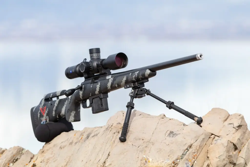Digital-camo precision rifle on the Atlas PSR BT46-LW17 bipod on rocks above a lake