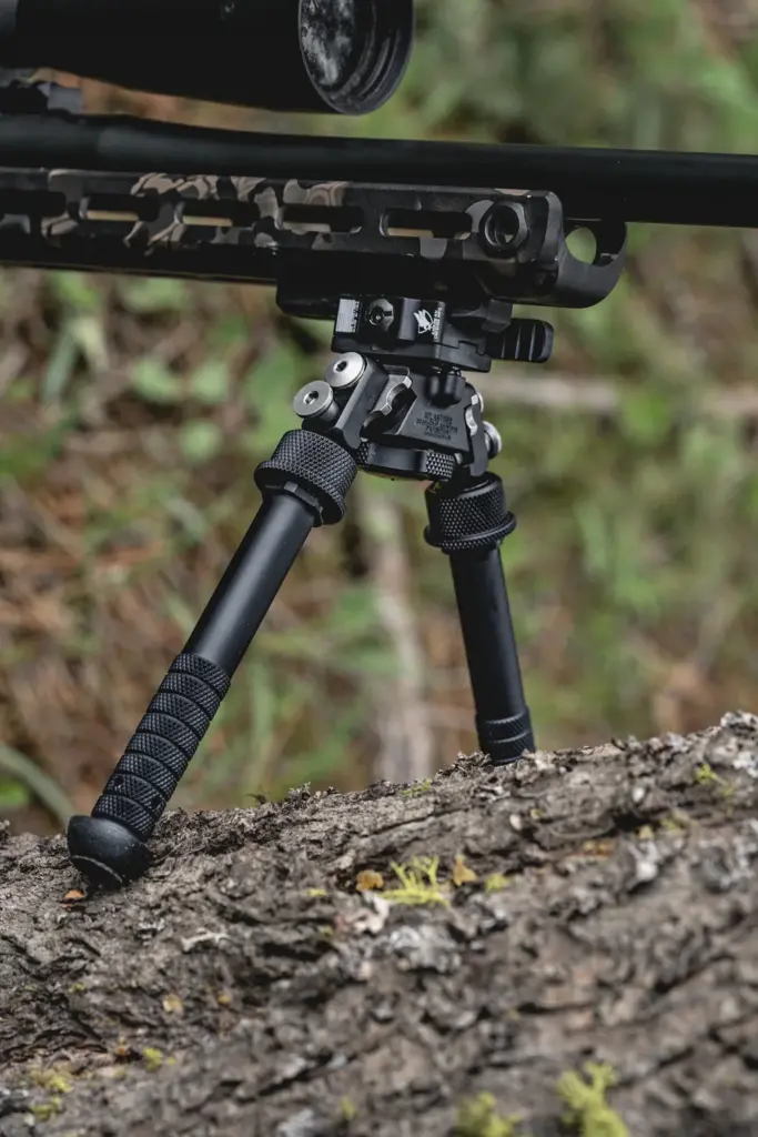 Close-up of Atlas PSR BT46-LW17 bipod legs deployed on a fallen log under an M-LOK camo rifle