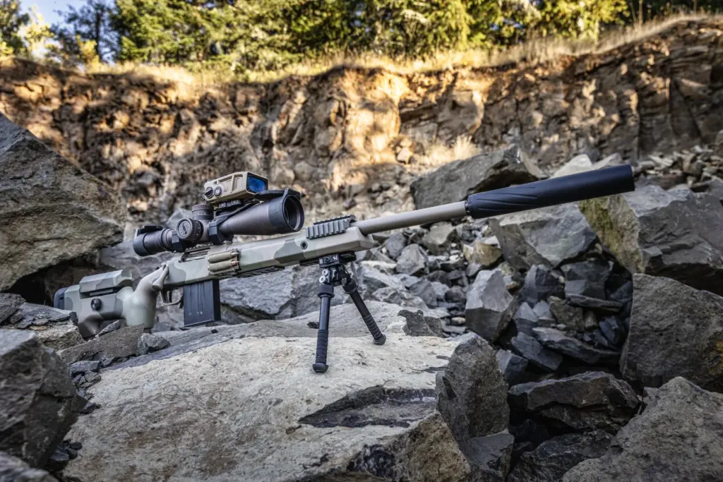 Tan suppressed bolt-action rifle deployed on the Atlas PSR BT46-LW17 bipod in a rock quarry